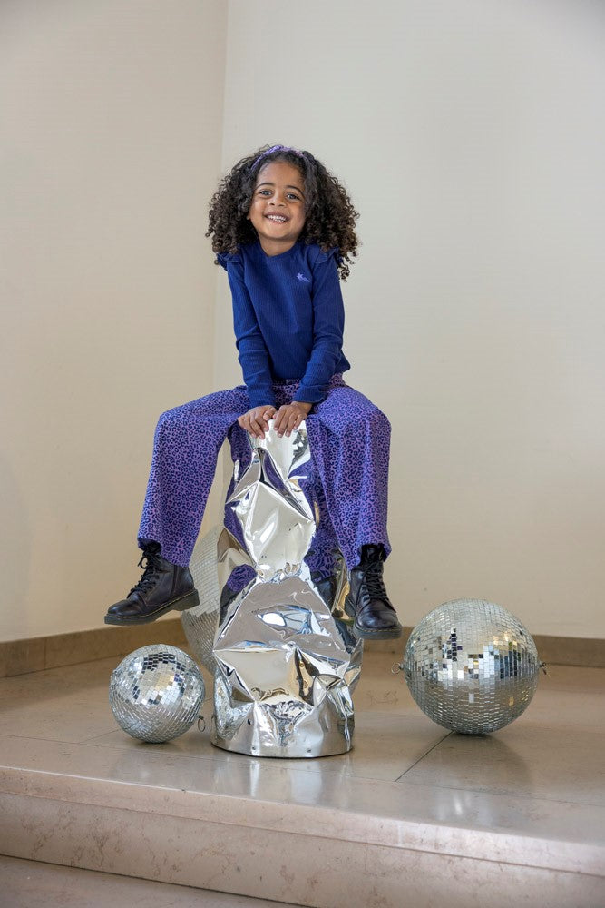 Jubel Flared Broek AOP - Wild Soul Sfeerfoto: "Kind draagt de Jubel Flared Broek AOP - Wild Soul in L.Lila, met vrolijke all-over print, perfect voor een winterwandeling of een speelse schooloutfit."