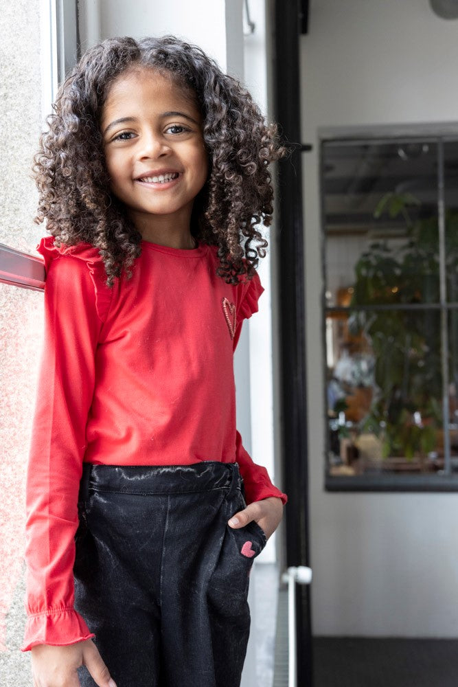 Jubel Longsleeve - Queen Of Hearts Sfeerfoto: "Kind draagt de Jubel Longsleeve - Queen Of Hearts in Rood, met een speelse hartprint, perfect voor een casual winteroutfit."