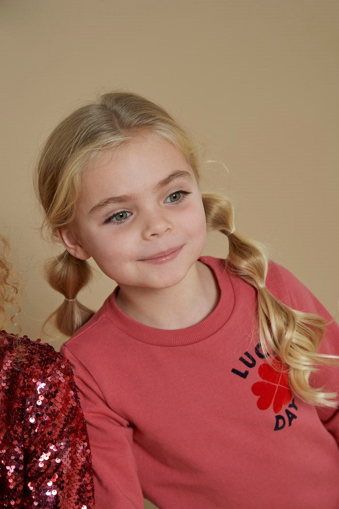 Jubel Sweater - Queen Of Hearts Sfeerfoto: "Kind draagt de Jubel Sweater - Queen Of Hearts in Roze, met een speelse hartprint, perfect voor een casual winteroutfit."