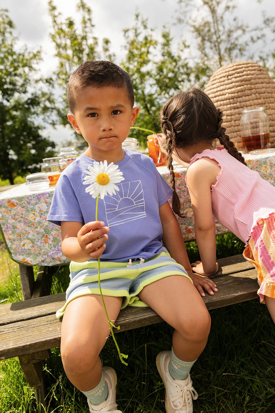 Jongentje met een Sproet & Sprout Raglan T-Shirt Sunrise aan en bloem in hand