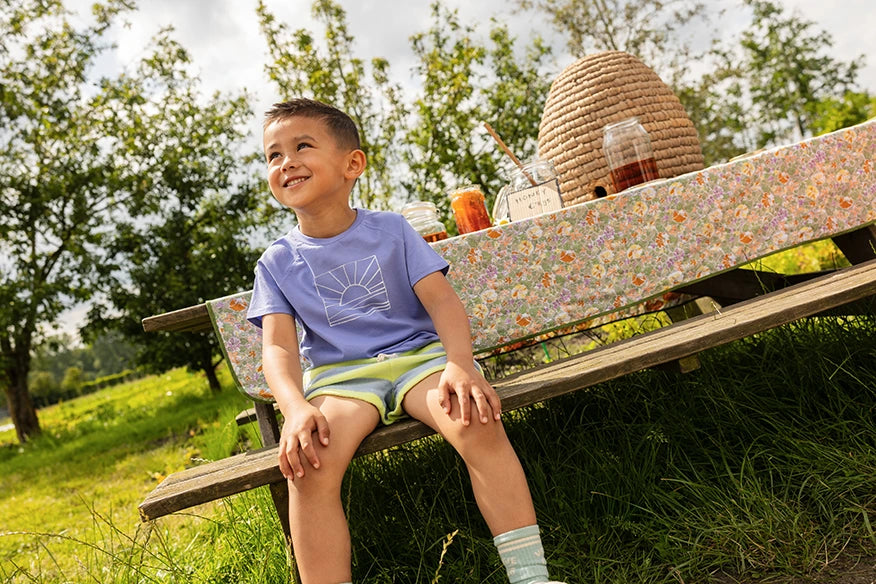 Jongen met een Sproet & Sprout Raglan T-Shirt Sunrise aan zit op bankje lacht