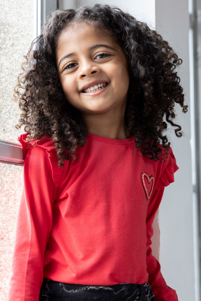 Jubel Longsleeve - Queen Of Hearts Sfeerfoto: "Kind draagt de Jubel Longsleeve - Queen Of Hearts in Rood, met een speelse hartprint, perfect voor een casual winteroutfit."