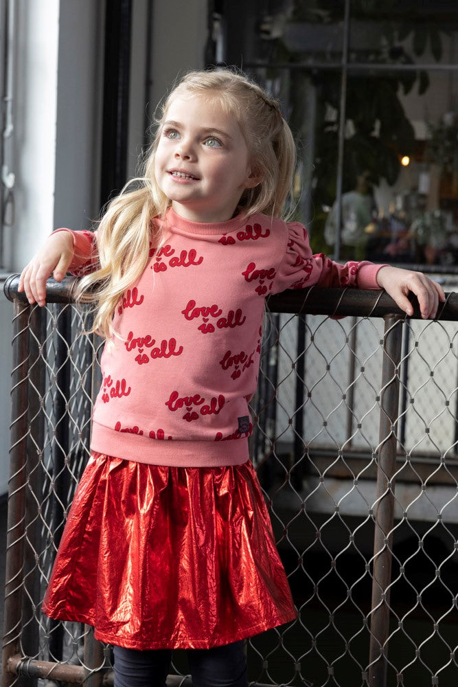 Jubel Sweater AOP - Queen Of Hearts Sfeerfoto: "Kind draagt de Jubel Sweater AOP - Queen Of Hearts in Lichtroze, met een speelse print van hartjes en strikjes, perfect voor casual winteroutfits."