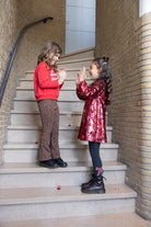 Jubel Flared Broek AOP - Queen Of Hearts Sfeerfoto: "Kind draagt de Jubel Flared Broek AOP - Queen Of Hearts in Bruin, met een speelse print van hartjes en strikjes, perfect voor casual winteroutfits."